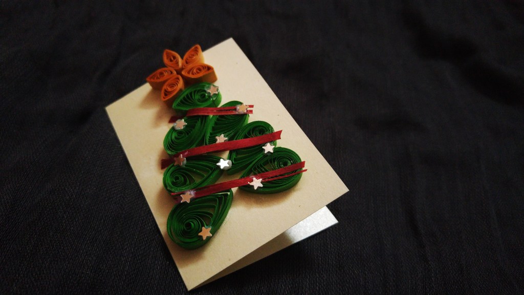 Swirled paper strips forming a green Christmas tree with an orange star, decorated with silver stars