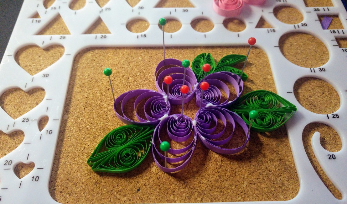 A purple quilling flower in progress on a cork board