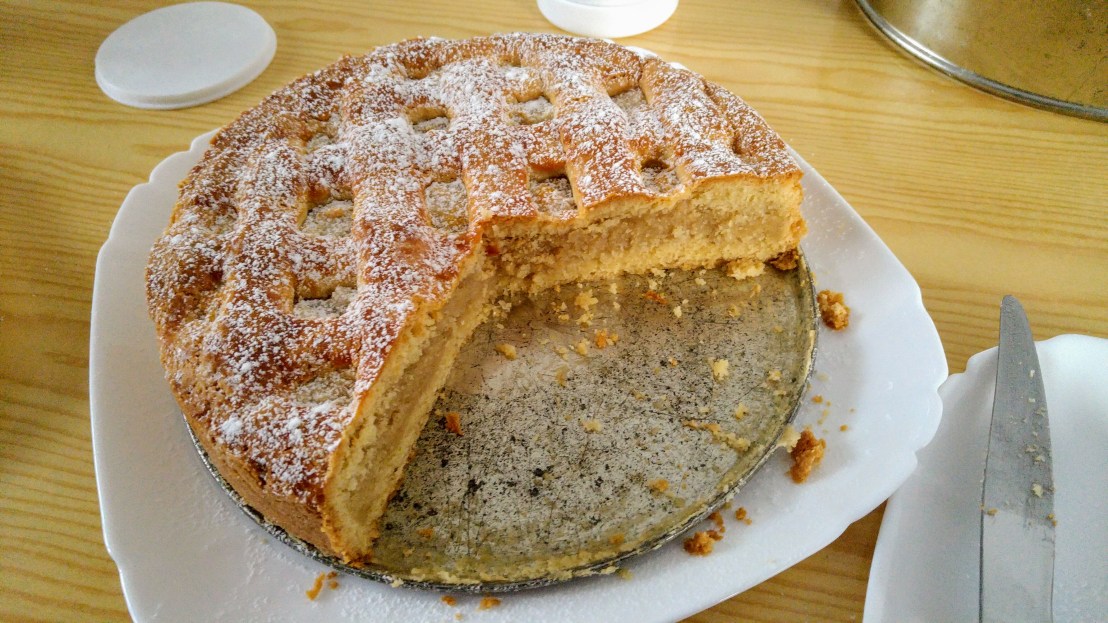 Almond cardamom tart on a plate, sliced into, dusted with icing sugar
