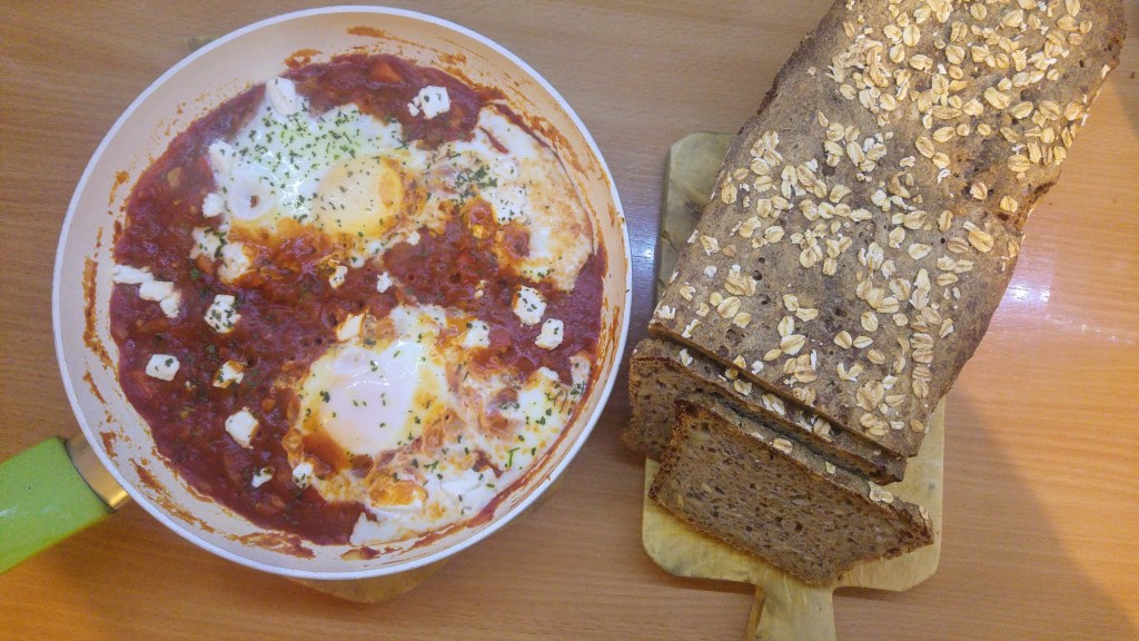 Cooked shakshuka in a pan and a loaf of sourdough bread