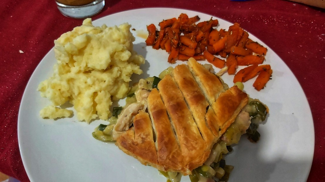 Chicken and leek pie on a plate with mashed potatoes and glazed carrots