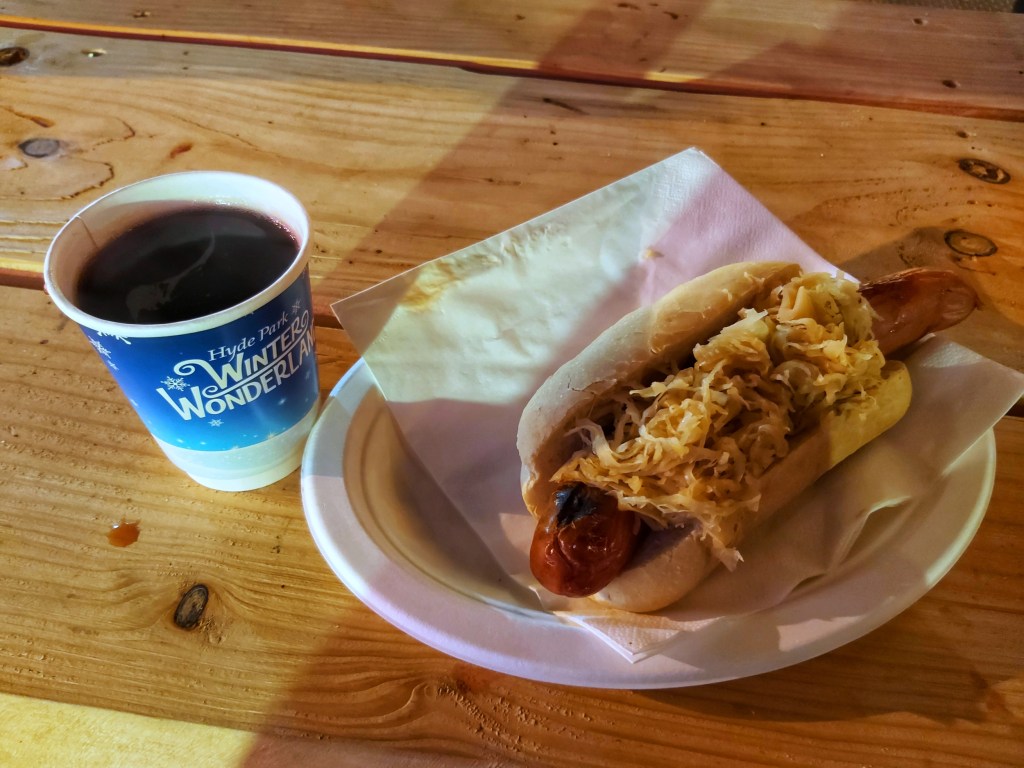A paper cup with mulled wine and a German sausage with sauerkraut.