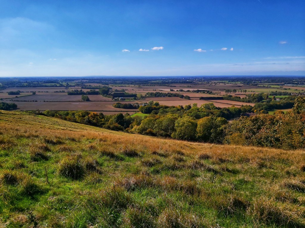 A view from the top of a hill in Kent Downs, near Wye. Autumnal landscape. Squares of fields on the horizon.