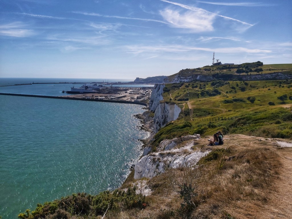 View from the top of white cliffs of Dover. Blue waters of the English Channel on the left. Large ferries visible further away.