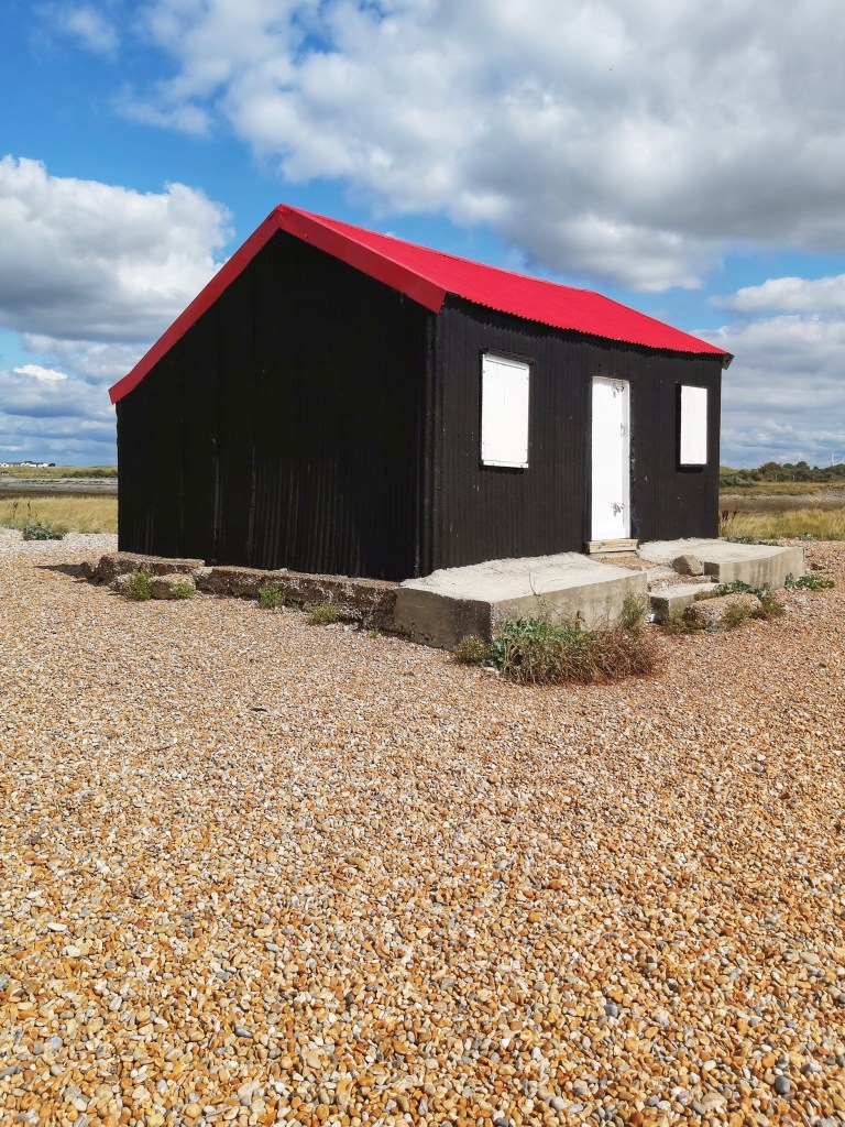 Red Roofed Hut in Rye Harbour Nature Reserve, on a pebbled beach.
