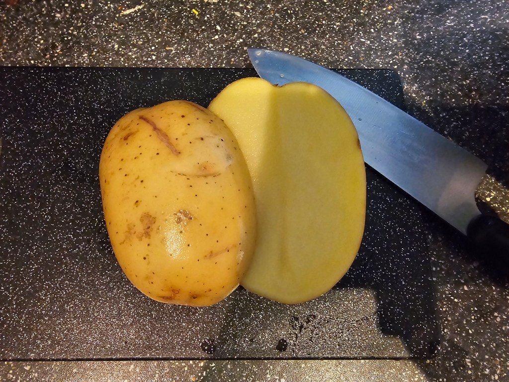A large baking potato sliced lengthways in half, on a chopping board