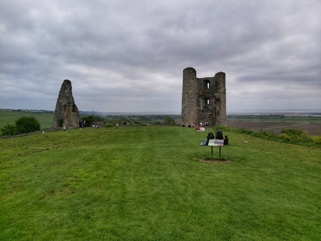 Ruins of Hadleigh Castle. Remains of two towers on top of a hill. Huge green meadow surrounding the ruins.