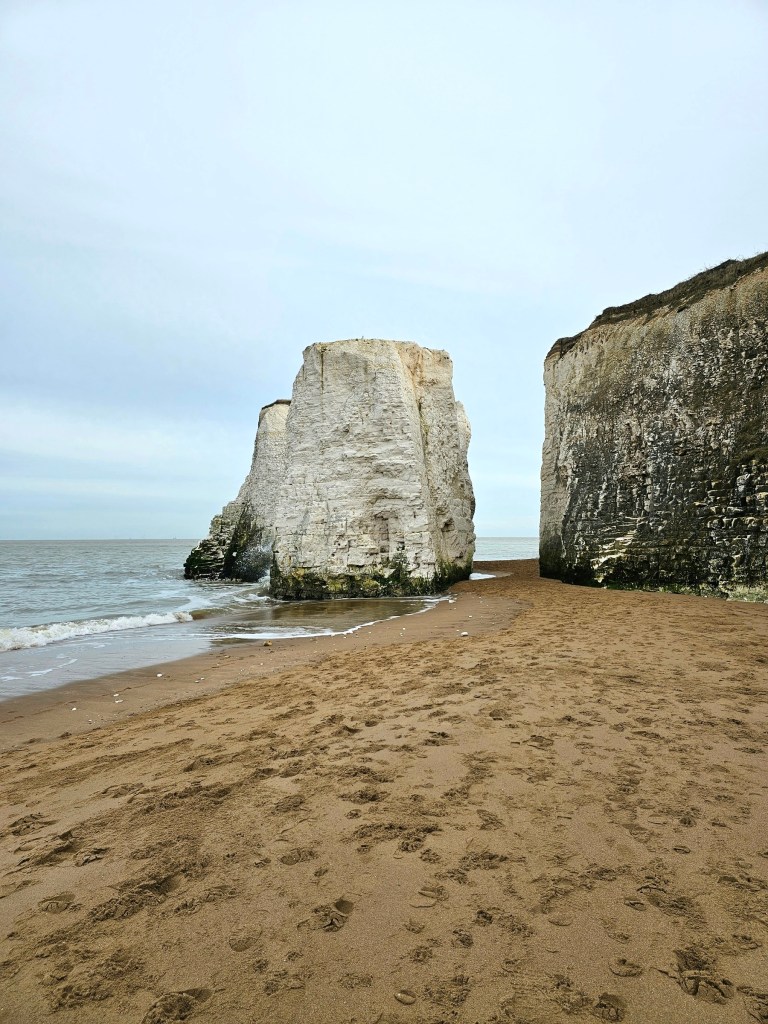 Pieces of free- standing white cliffs detached from the main cliff on a sandy beach in Botany Bay Beach, Kend, England. The sea is gently washing the bottom of the rocks.