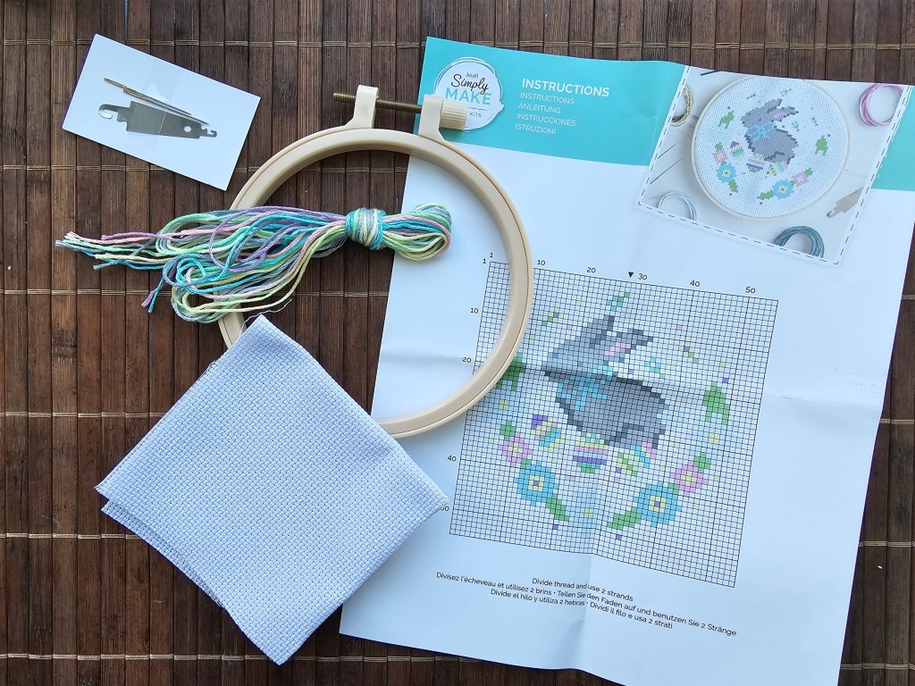 The contents of an Easter Bunny sross stitch kit - a hoop, a blank aida, needle and threader, assorted yarns and a leaflet with instructions.
