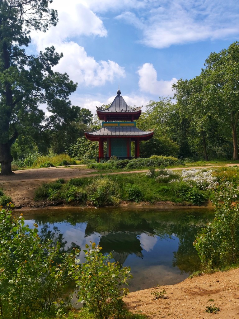 Chinese pagoda in Victoria Park, London. Overlooking a small pond, surrounded by grass and trees.