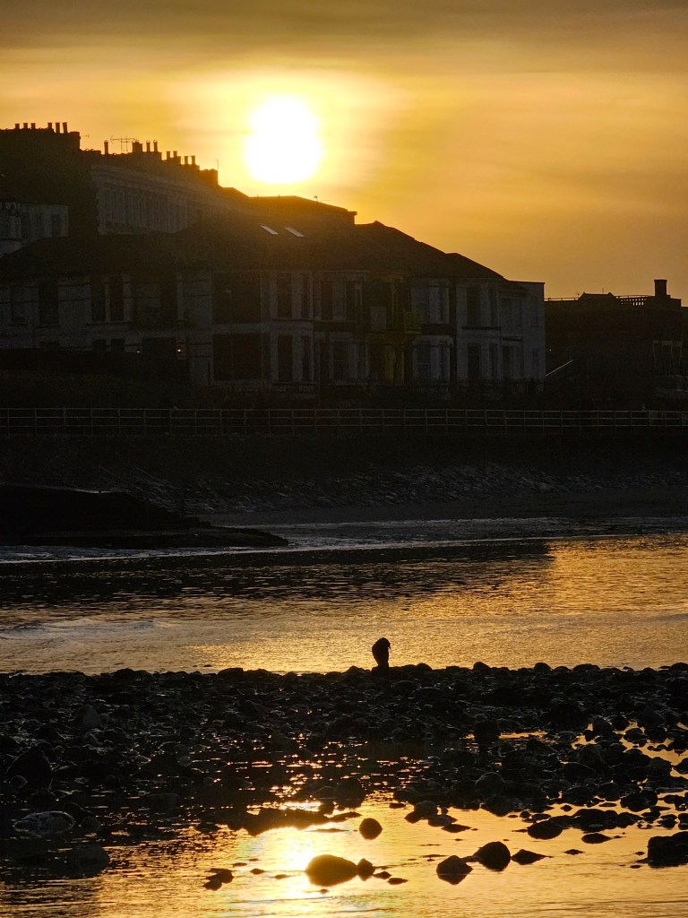 Sunset in Margate. The sun is setting over the rooftops of Margate houses. The sunset light reflected in the water on the beach.