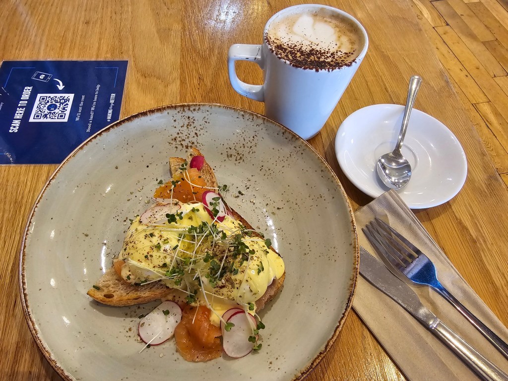 Lunch at Boston Tea Party Cafe in Salisbury. Poached eggs with hollandaise sauce, sliced radishes and smoked salmon, served on sourdough. A mug of cappuccino.