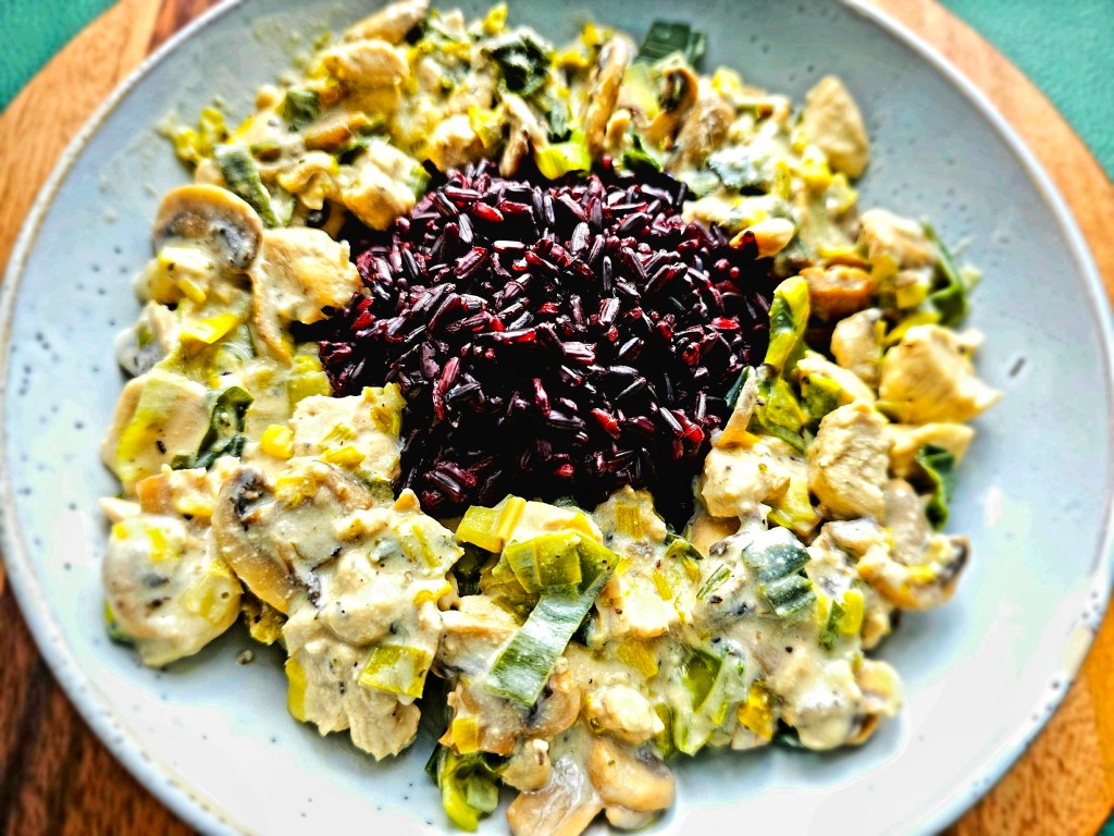 Creamy Chicken In Leek And Mushroom Sauce on a pale blue plate. Served with a pile of black rice.