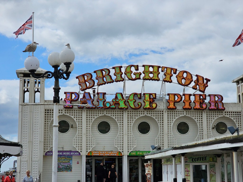 Brighton Palace Pier game arcade. Two seagulls sitting on a lamppost. British flag waving on the wind.