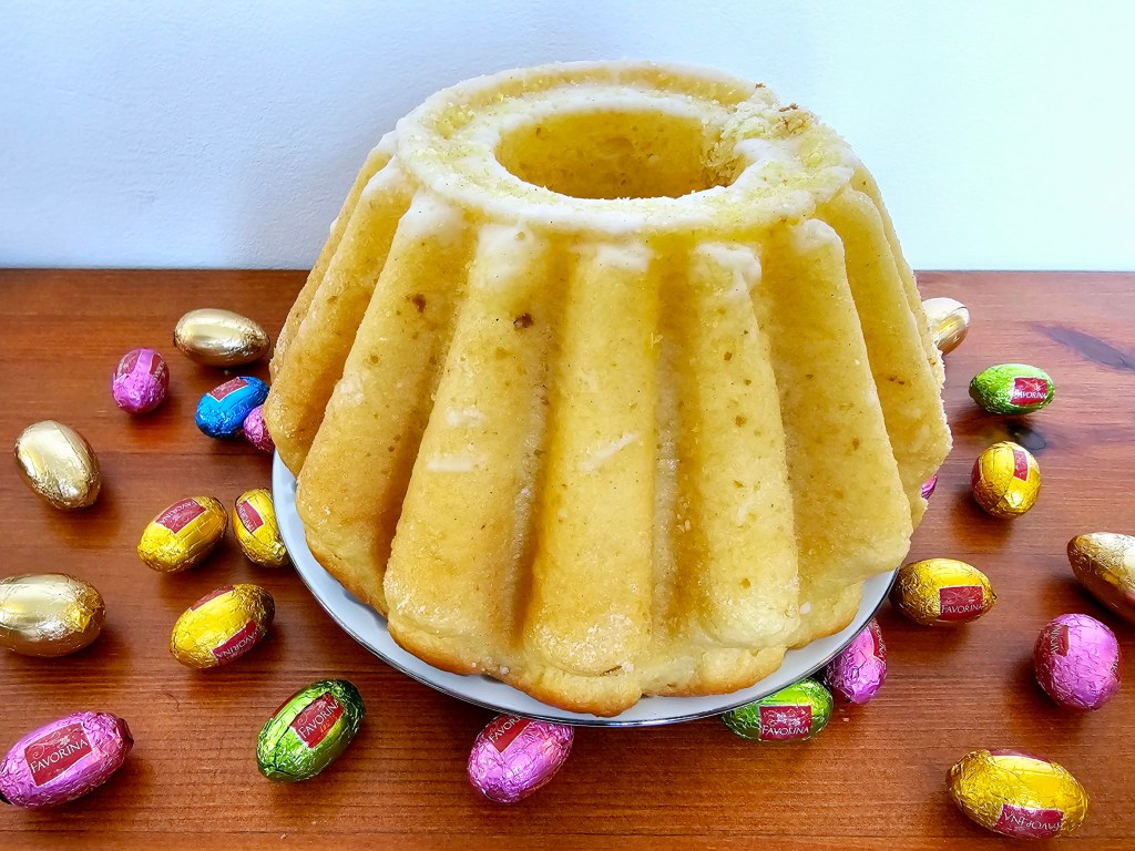 Polish Easter cake - lemon babka. The cake is placed on a plate. There are foil-wrapped chocolate eggs around the cake.