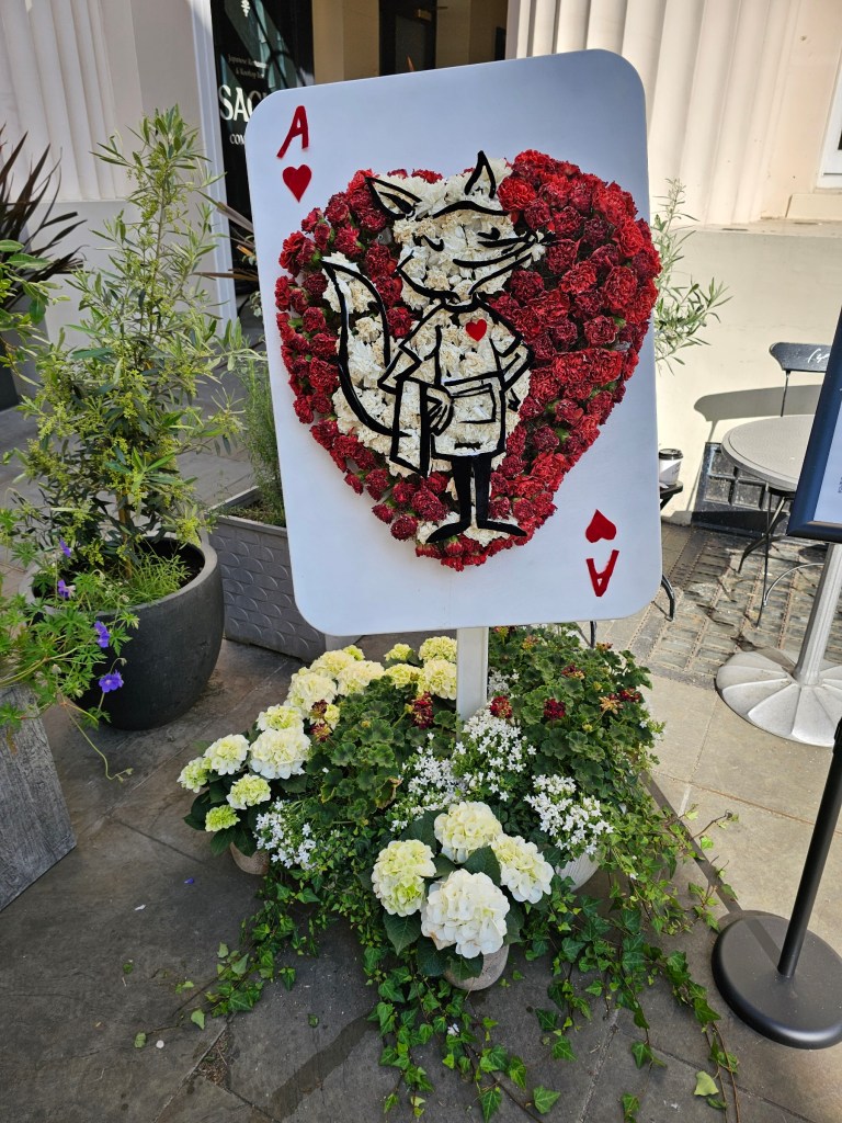 A playing card sign made of fresh red and white flowers in front of a restaurant in Belgravia, London.