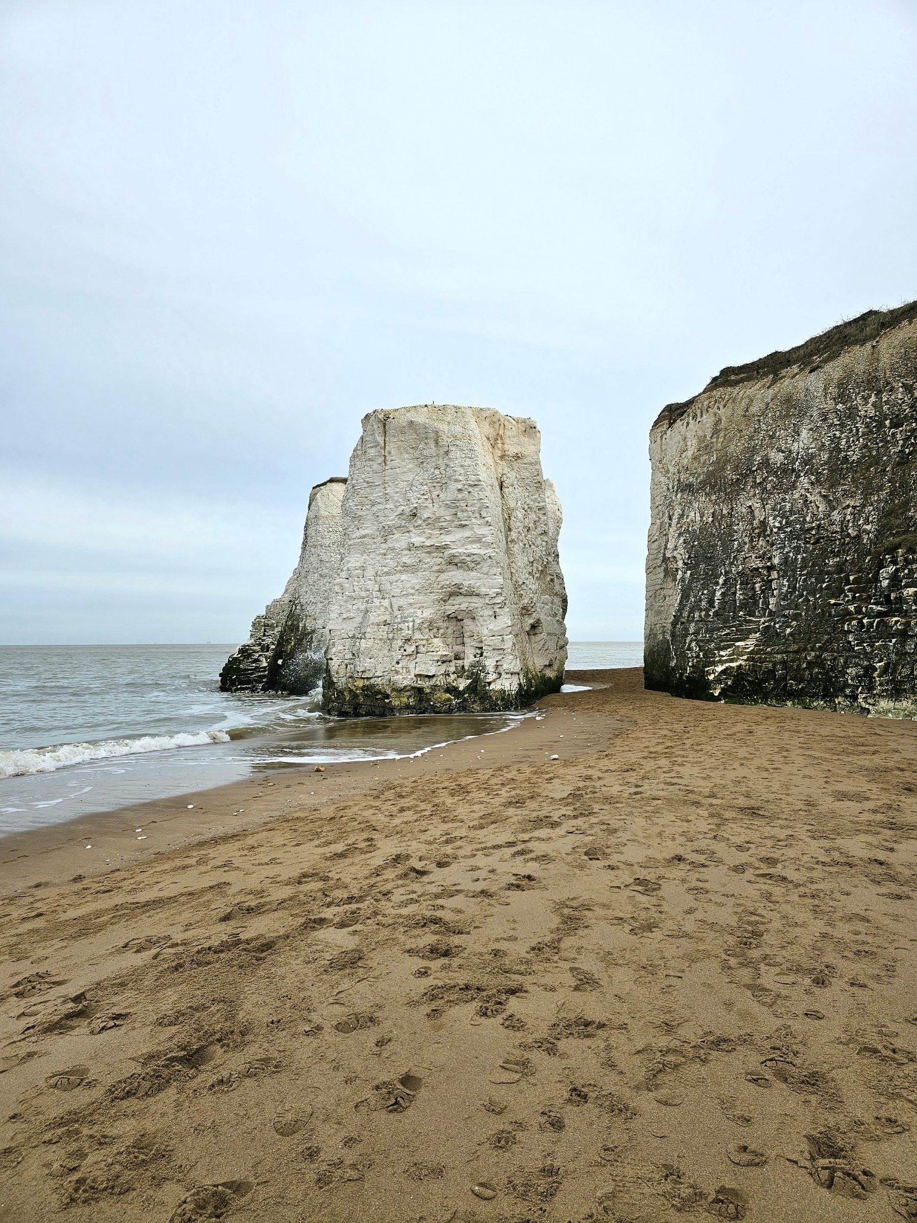 Pieces of free- standing white cliffs detached from the main cliff on a sandy beach in Botany Bay Beach, Kend, England. The sea is gently washing the bottom of the rocks.