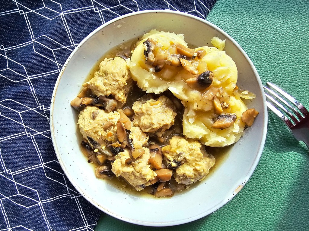 A plate with five chicken meatballs, mashed potatoes and mushroom gravy.