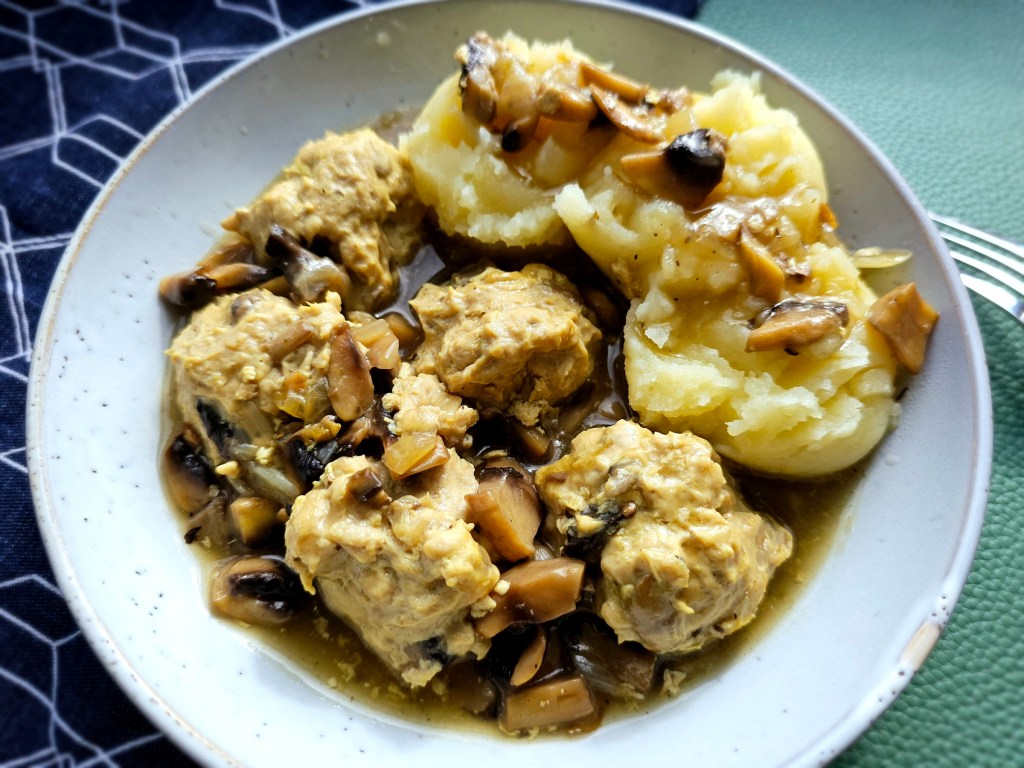 A plate with five chicken meatballs, mashed potatoes and mushroom gravy.