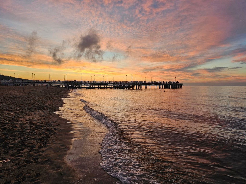 Sunset at a beach in Gdańsk, near Brzeźno pier. Golden-orange skies with a few clouds and gentle ripple on the surface of the Baltic Sea.
