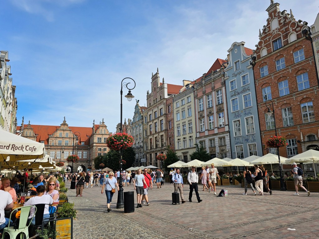 The centre of Gdańsk Old Town. Colourful building facades, rows of coffee shops and tourists strolling around.