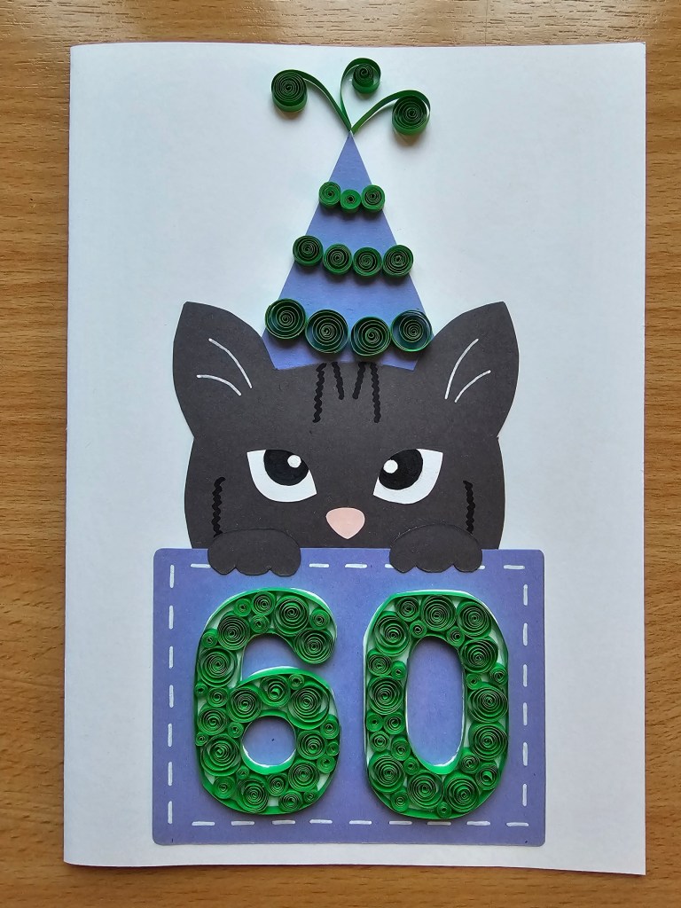 Scrapbooking card - cat - with quilled elements. The cat is wearing a birthday hat and is holding a sign with the number 60.