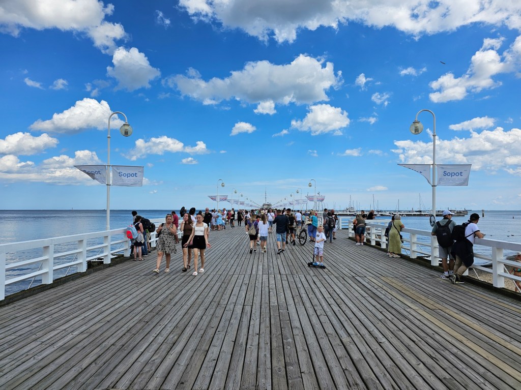 Sopot Pier - the longest wooden pier in Europe. You can see blue skies and lots of tourists.