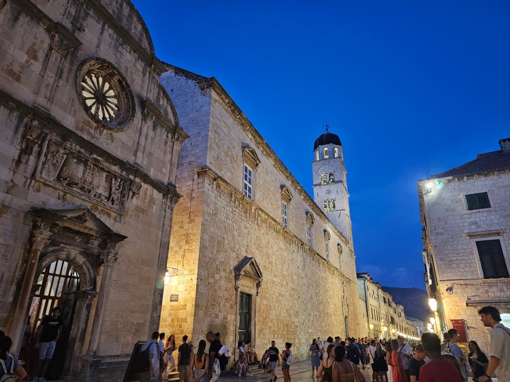 Dubrovnik Old Town in the evening. The light stone buildings are lit up.
