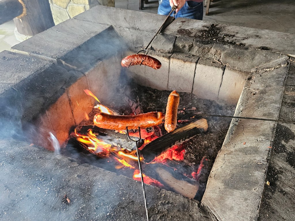 Three sausages being roasted over a fireplace.