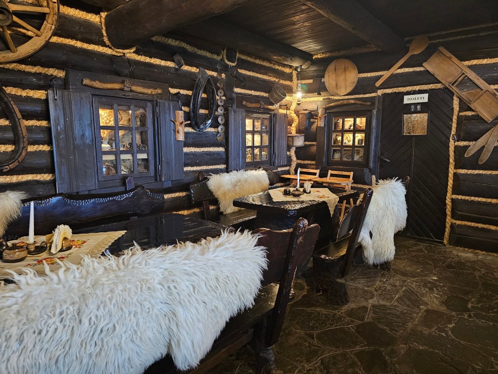 Traditional interior design of a restaurant on Mount Równica. The walls are covered with wooden panels and there are sheepskins on the seats.