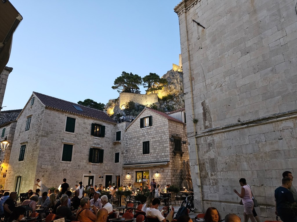 Omiš Old Town bustling with life at night. Restaurants are full of diners, and the buildings are lit up.