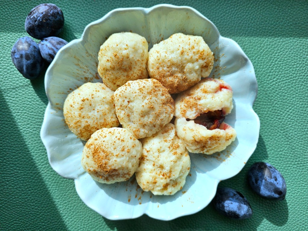Cooked plum dumplings, Polish knedle, served on a round plate and sprinkled with cinnamon. One of the dumplings is cut open.