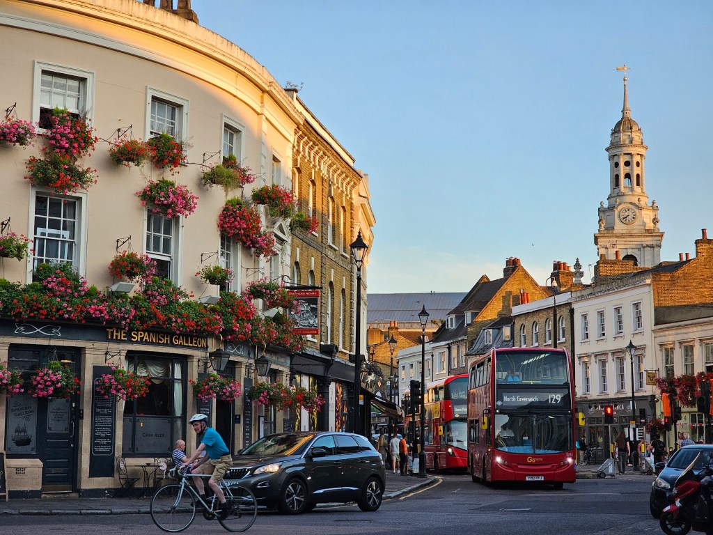 A pub adorned with fresh flowers and a red double-decker bus in Greenwich, London.