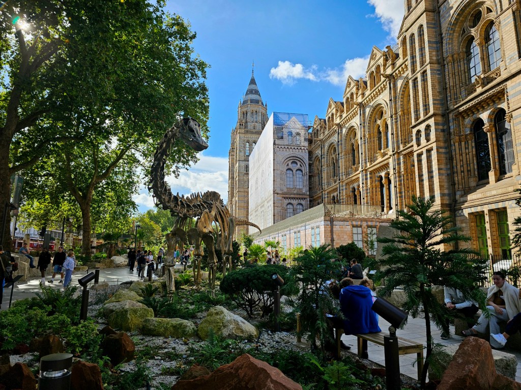 The new gardens in front of Natural History Museum in London, featuring a large statue of a dinosaur skeleton.