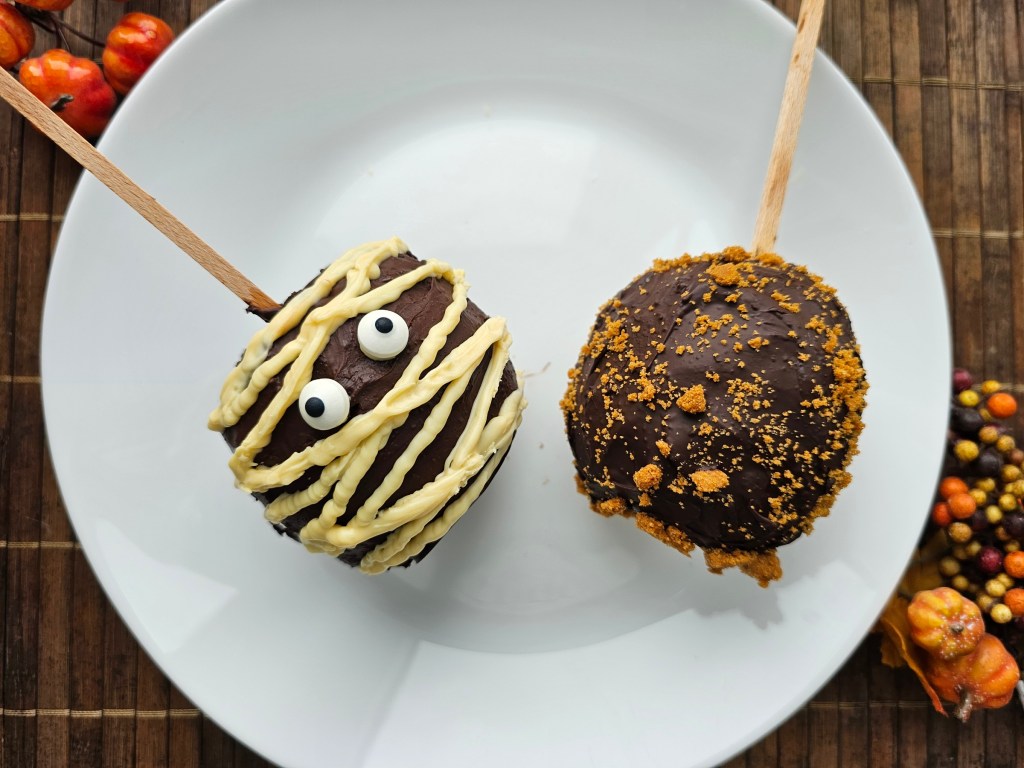 Two homemade chocolate coated apples for Halloween - a mummy apple and a Biscoff apple.