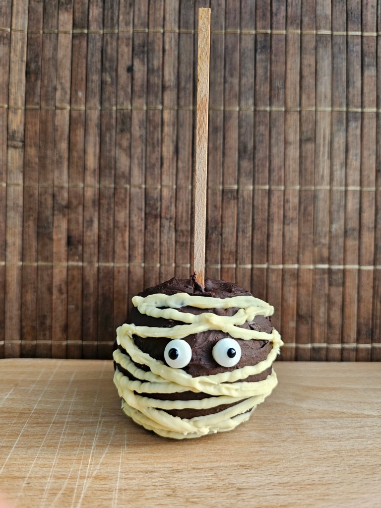 A Halloween chocolate coated apple on a stick, with white chocolate decoration making it look like a mummy.