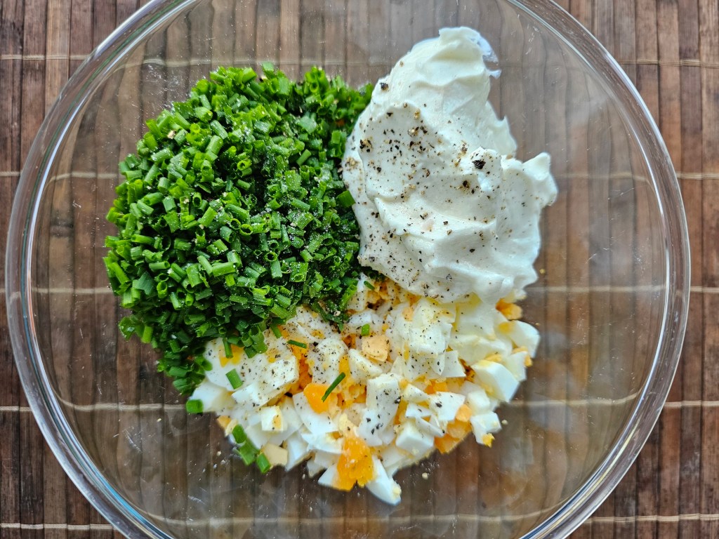 Chopped up hard boiled eggs, chives and cream cheese in a glass bowl.