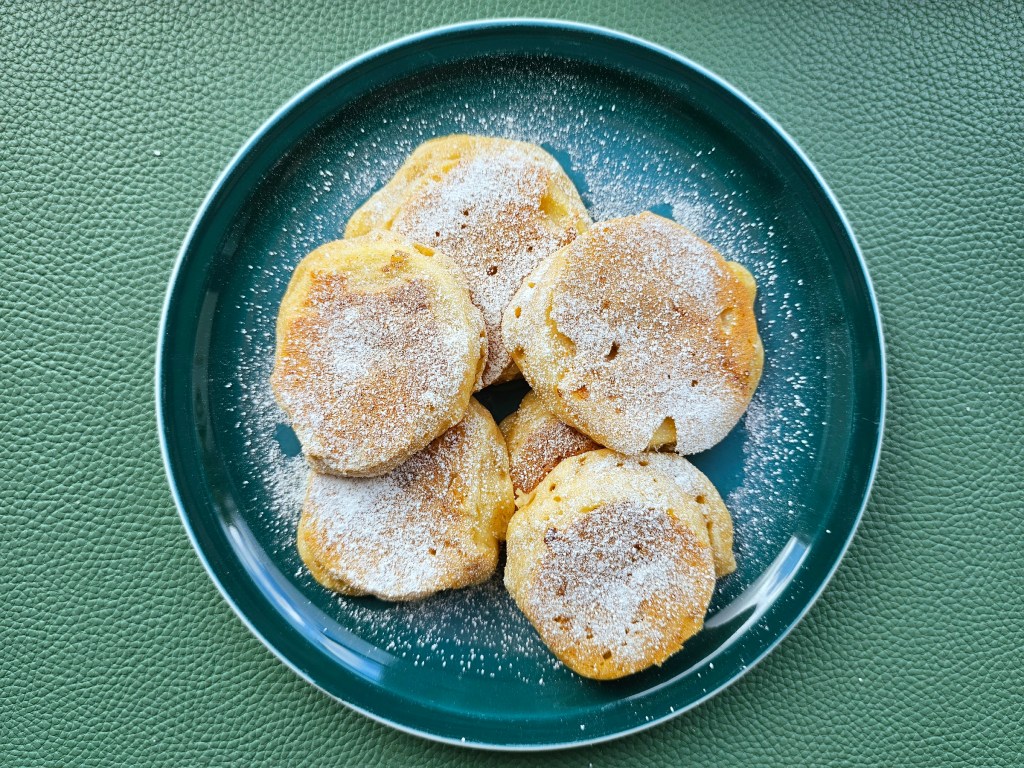 Bird's view of a plate with a pile of high protein apple fritters dusted with icing sugar.