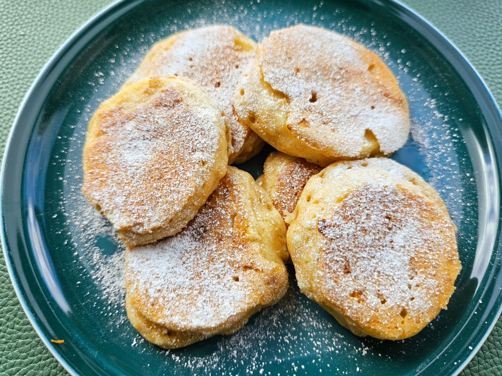 A plate with a pile of healthy apple fritters dusted with icing sugar.