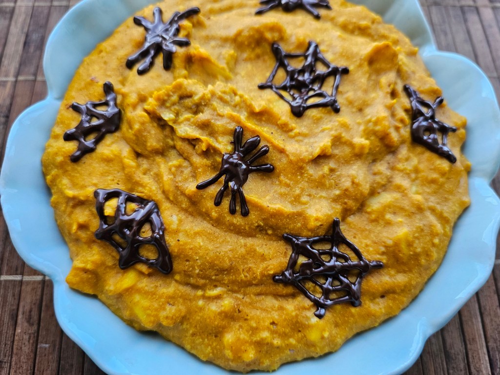 A bowl of pumpkin spice porridge with chocolate decorations on top - chocolate spiders and spiderwebs.