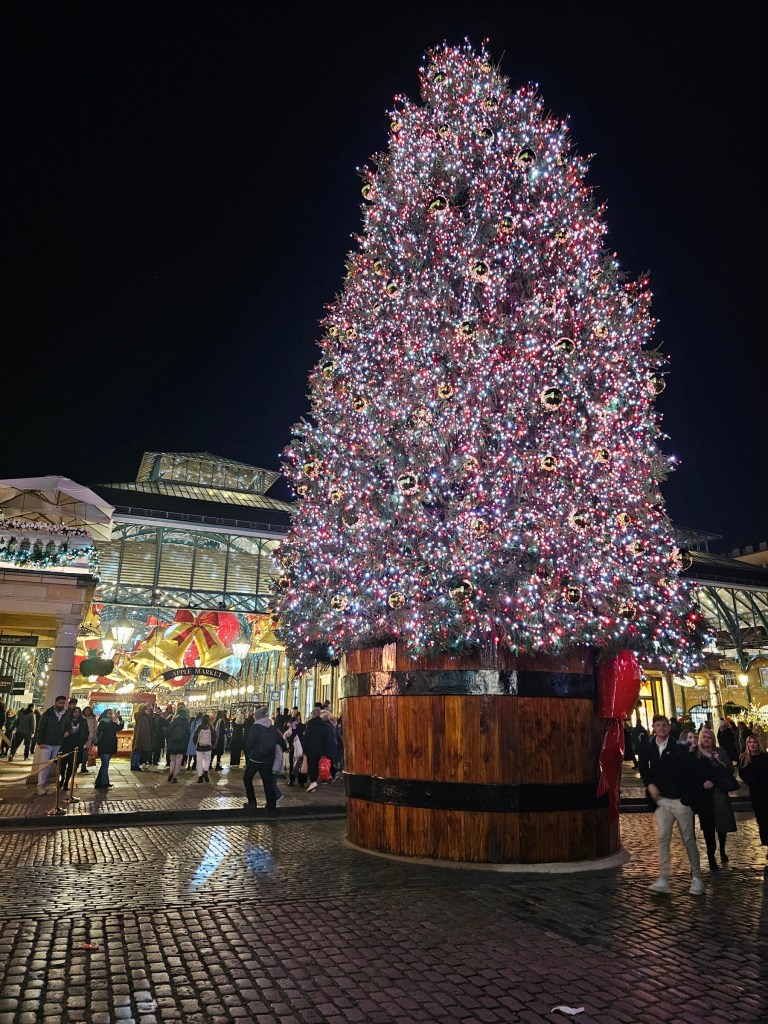 Large Christmas Tree in Covent Garden, London, in 2024. The tree is illuminated with red lights.
