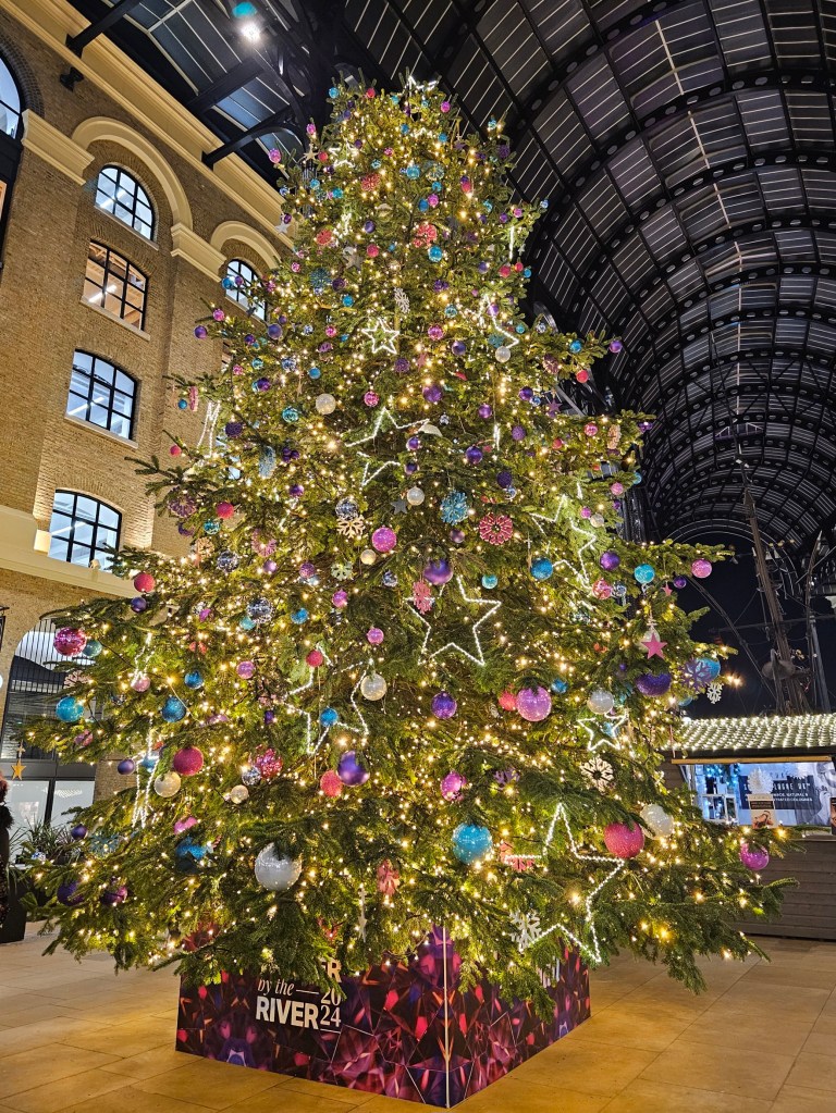 A large Christmas tree with fairy lights and pink, purple and blue baubles, in Hay's Galleria in London.