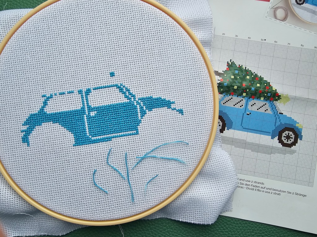 Partially finished cross stitch project depicting a car transporting a Christmas Tree. The blue parts are nearly done.