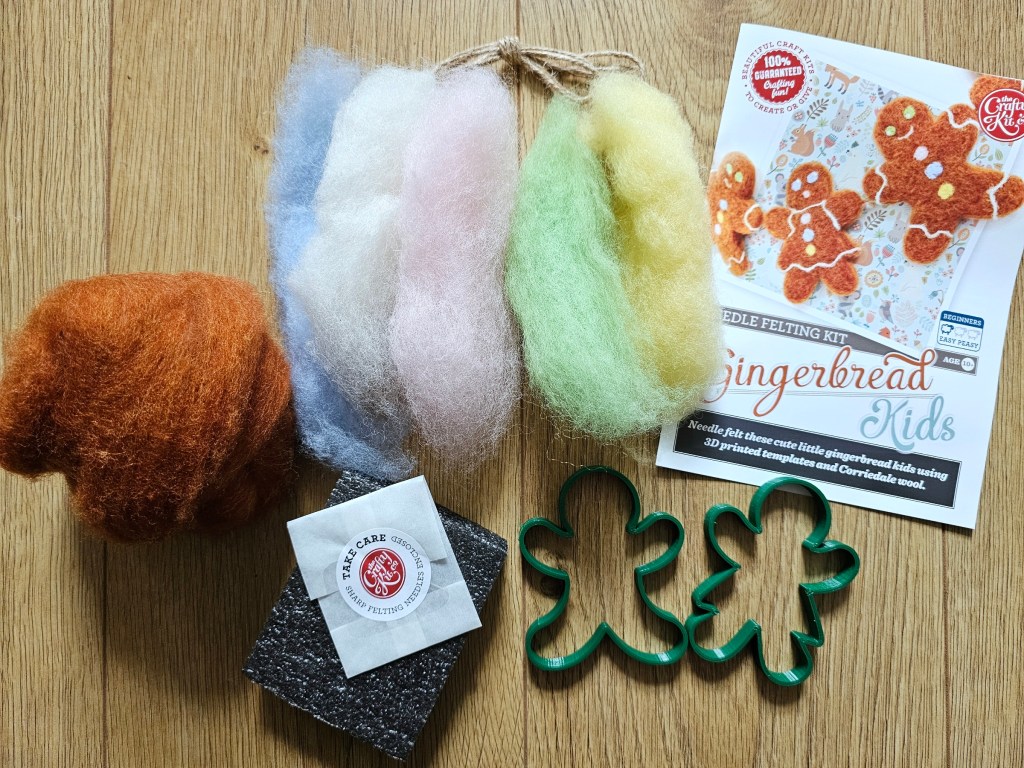 Content of the box for creating needle felted gingerbread men. The box includes wool in five colours, a felting mat, two moulds, two needles and a leaflet with instructions.