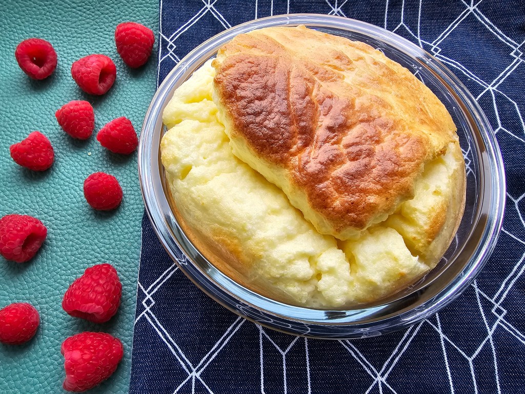 Baked high protein cheesecake souffle in an ovenproof dish, next to a handle of fresh raspberries.