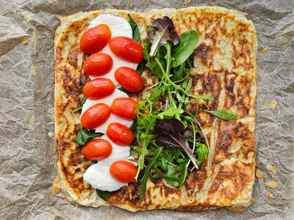 Baked gluten free high protein cottage cheese wrap, with mozzarella, tomatoes and salad leaves.