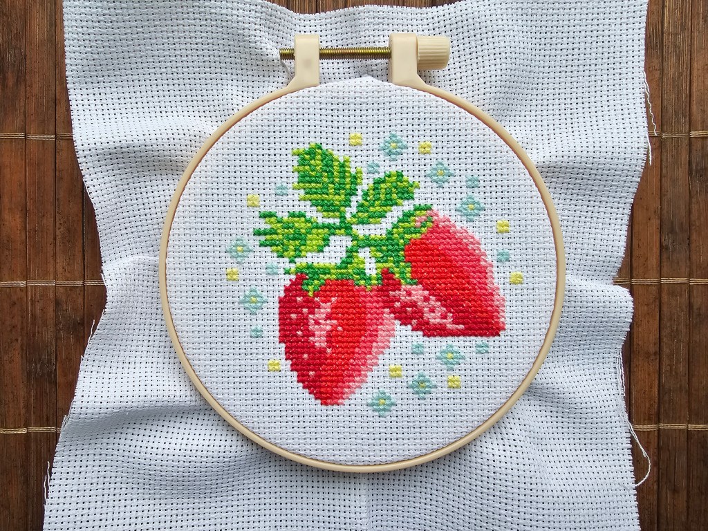 Finished cross stitch design featuring two strawberries and small blue and yellow flowers.