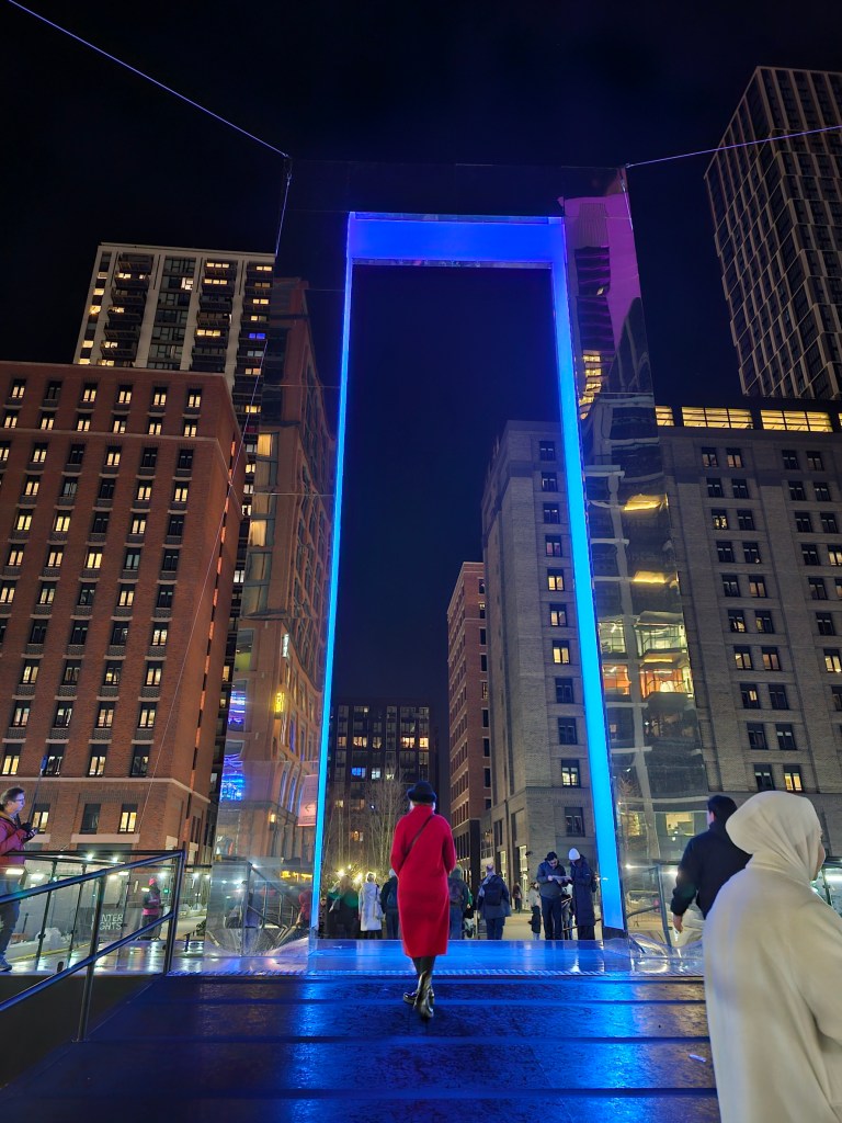 A tall, illuminated gate looking like a portal in the middle of a city.