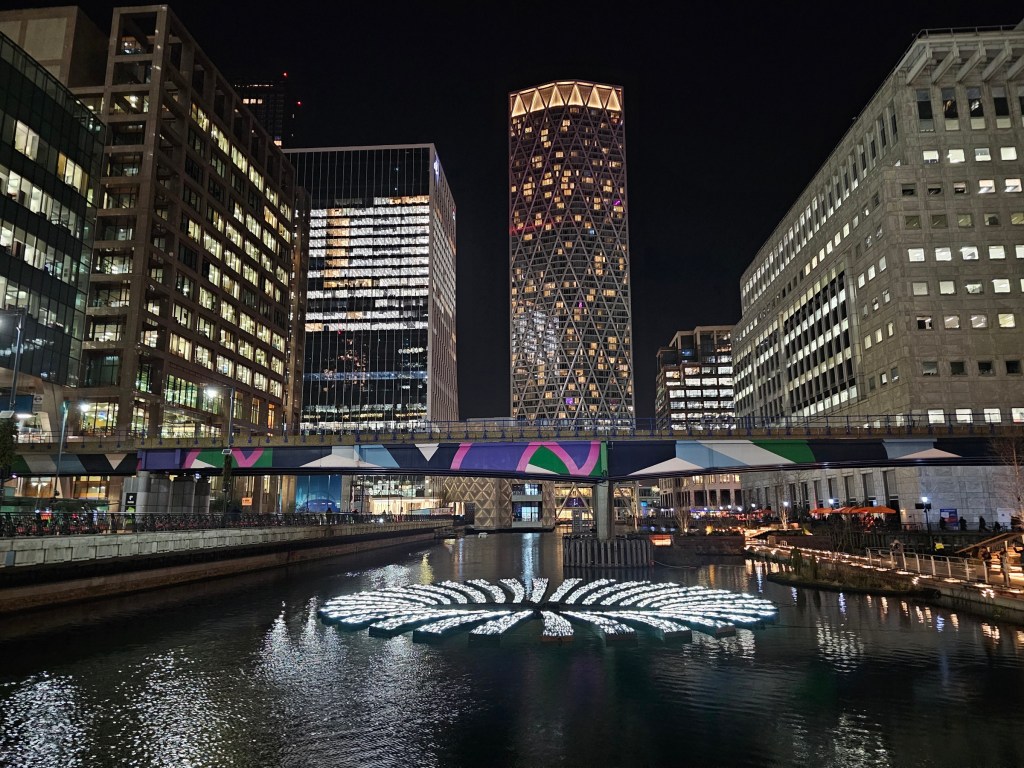 A lights installation looking like a sinkhole, located on a canal in an area filled with skyscrapers.