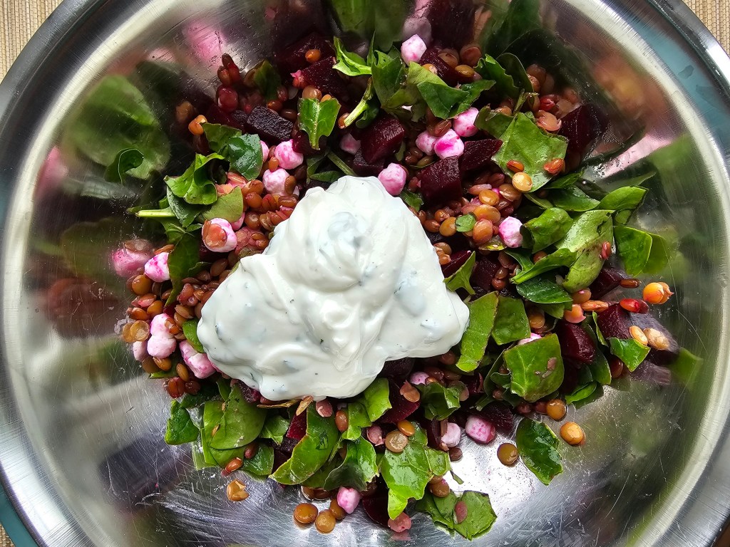 Baby spinach, cooked green lentils and wheatberries, goat's cheese and pickled beetroot in a metal bowl. Topped with mint yoghurt dressing.